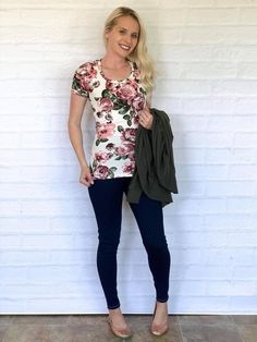 a woman standing in front of a white wall wearing black pants and a floral top