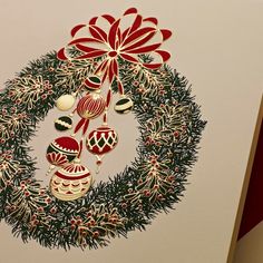 a christmas wreath with ornaments hanging from it's side on a white wall next to a red ribbon