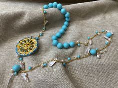 ✔️ Gorgeous Sicilian style necklace! Composed of hand-knotted turquoise paste beads, bottom ring with gold-plated stainless steel chain, white and turquoise pearls and scaramazza pearls. The whole thing is completed by a Sicilian cart wheel in Caltagirone ceramic, hand painted. Perfect jewel to enrich a casual outfit or for an important moment! Wear the Sicilian tradition with this necklace! ✔️DETAILS: 🟩 Materials: Turquoise paste Stainless steel Gold Pearls Caltagirone ceramics 🟧🟧Dimensions: Turquoise Beaded Necklace With Pearl Charm As Gift, Gift Turquoise Necklaces With Pearl Chain, Turquoise Beaded Necklaces With Pearl Chain As Gift, Gift Turquoise Beaded Necklace With Pearl Chain, Turquoise Pearl Necklace As A Gift, Sicilian Style, River Pearls, Ceramic Hand, Style Necklace