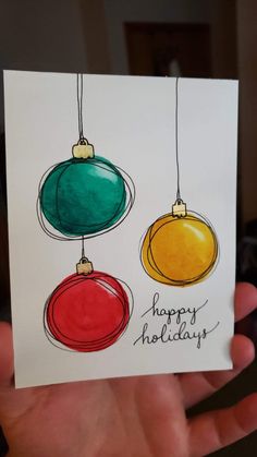 a hand holding up a card with three christmas ornaments hanging from it's sides