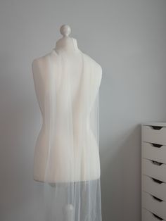 a white mannequin covered in sheer fabric next to a dresser with drawers on it