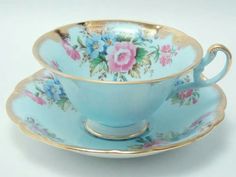 a blue tea cup and saucer with pink flowers on the rim, sitting side by side