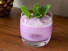 a purple drink with mint garnish in a glass on top of a wooden table