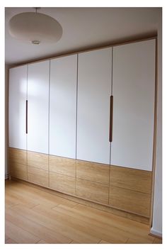 an empty room with white cupboards and wood flooring on the wall, in front of a window