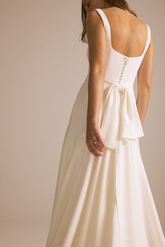 a woman in a white dress with a bow on the back and her hands behind her back