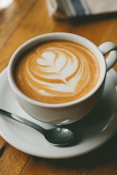 a cappuccino on a saucer with spoons sits on a wooden table