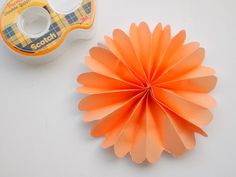 an orange paper flower next to a tape dispenser on a white surface