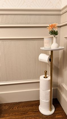 a toilet paper holder with two rolls of toilet paper on it and a vase with an orange flower