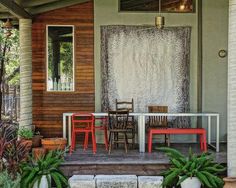 an outdoor dining area with red chairs and green plants on the front porch next to a door