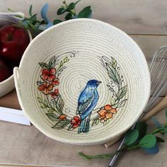 a blue bird sitting on top of a bowl next to an apple and whisk