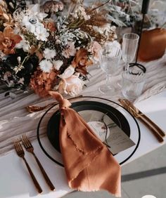 the table is set with an orange napkin and silverware, along with a bouquet of flowers