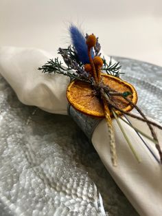 an orange slice on a napkin with some dried herbs sticking out of it and sitting on top of a silver plate