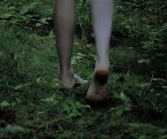 a person walking in the woods with their bare feet on the grass and trees behind them