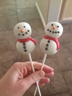 two snowman lollipops are being held by someone's hand on the tile floor