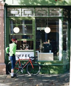 a woman standing next to a bike in front of a coffee shop