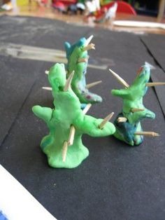 three green dinosaur figurines sitting on top of a black surface with toothpicks sticking out of them