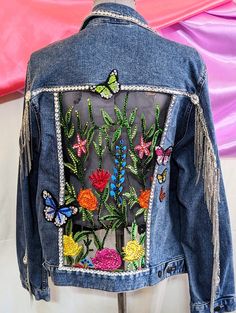 a denim jacket with embroidered flowers and butterflies on the back, sitting on a mannequin