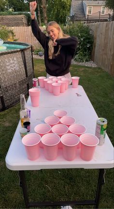 a woman standing in front of a table filled with pink cups and drinks on top of it