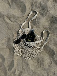 a white bag sitting on top of a sandy beach next to a bottle and comb