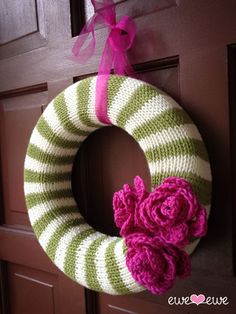 a green and white striped knitted wreath with pink flowers hanging on the front door