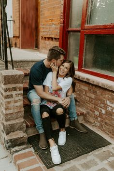 a man and woman are sitting on the steps together, smiling at each other as they hug