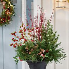 a vase filled with red berries and greenery on top of a table next to a door