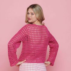 a woman standing in front of a pink wall wearing a pink crochet sweater