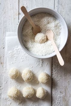 some food is in a white bowl on a wooden table with spoons and rice balls