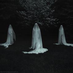 three ghostly people standing in the dark with white veils on their heads and body