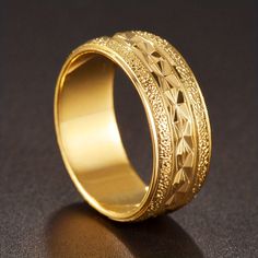 a gold wedding ring with intricate designs on the outside and inside, sitting on a black surface