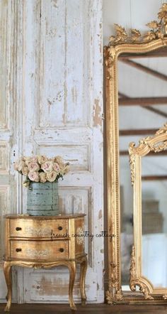 an antique dresser with flowers in a vase on top and a large mirror behind it