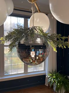 a disco ball hanging from the ceiling in front of a window with greenery on it