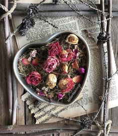 a heart shaped bowl filled with dried flowers on top of an open book next to branches