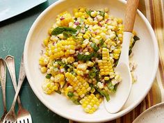 a white bowl filled with corn on top of a table next to utensils