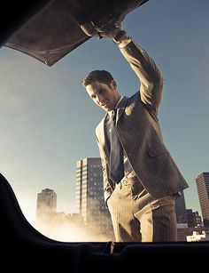 a man in a suit and tie is holding his car hood up to the side