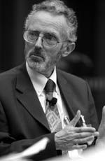 black and white photograph of a man in suit sitting at a table with his hands folded out