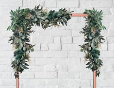 two copper frames with greenery on them against a white brick wall in the shape of an arch