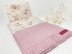 a pink blanket and pillow sitting next to each other on a white surface with flowers