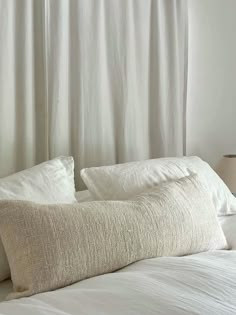 a white bed with two pillows on top of it next to a lamp and window