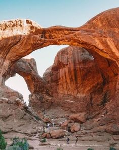 an arch in the side of a mountain with people standing under it and some trees