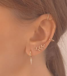 a close up view of a woman's ear wearing gold earrings with leaves on them