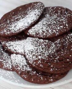 chocolate cookies with powdered sugar on top sit on a white plate, ready to be eaten