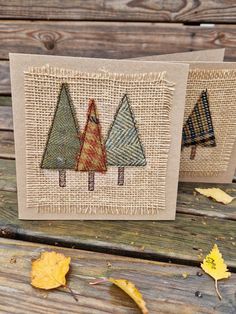 two small cards with trees on them sitting on a wooden table next to autumn leaves