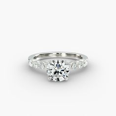 a white gold engagement ring with diamonds on the band and a round brilliant cut center stone