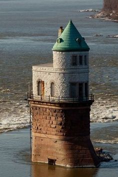 a tower with a green roof sitting in the middle of a body of water next to a cliff