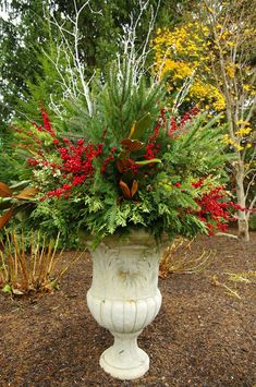 a white urn filled with lots of flowers and greenery next to shrubbery