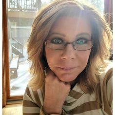 a woman with glasses is looking at the camera while sitting in front of a window