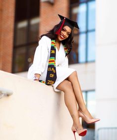 a woman sitting on top of a wall wearing a graduation cap and gown