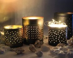 three lit candles sitting on top of a table next to rocks and shells in front of them