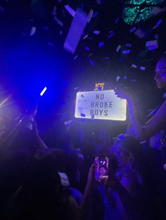 a group of people holding up cell phones in front of a sign that says no broke boys